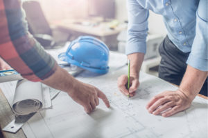Two men looking at blueprint with hard hat on table
